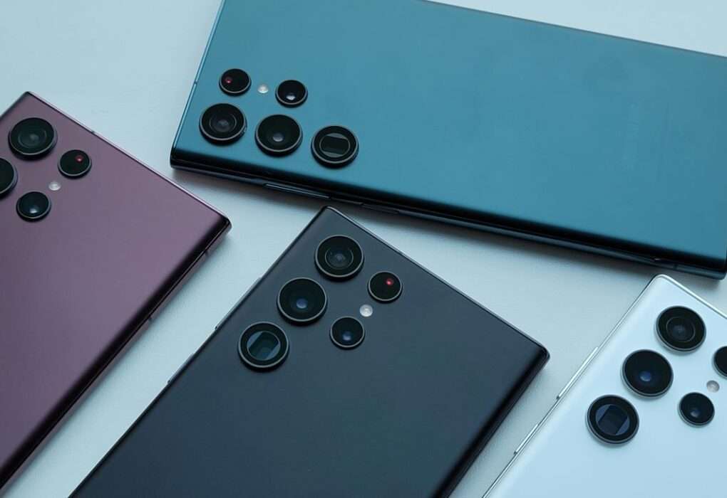 Four Samsung Galaxy S22 Ultra smartphones in different colors (burgundy purple, black, white, and green-blue) laid out on a white background, viewed from the back to highlight the distinctive five-lens camera module.